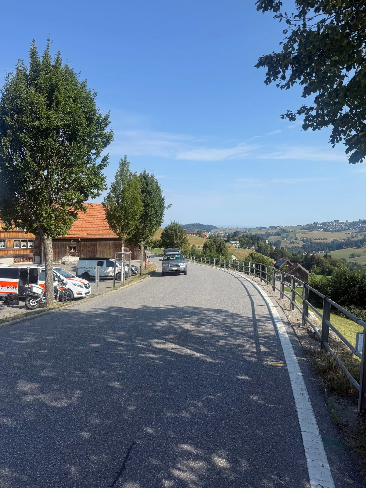 Mehrere Polizeifahrzeuge stehen an einer Landstraße neben einem Bauernhaus. Im Hintergrund sind Hügel zu sehen.