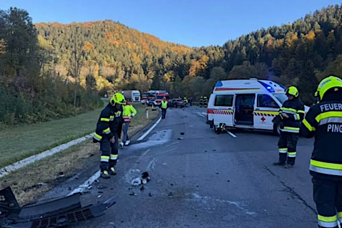 Mehrere Feuerwehrleute arbeiten an einer Unfallstelle auf einer Landstraße. Ein Rettungsfahrzeug steht mit offener Tür bereit.