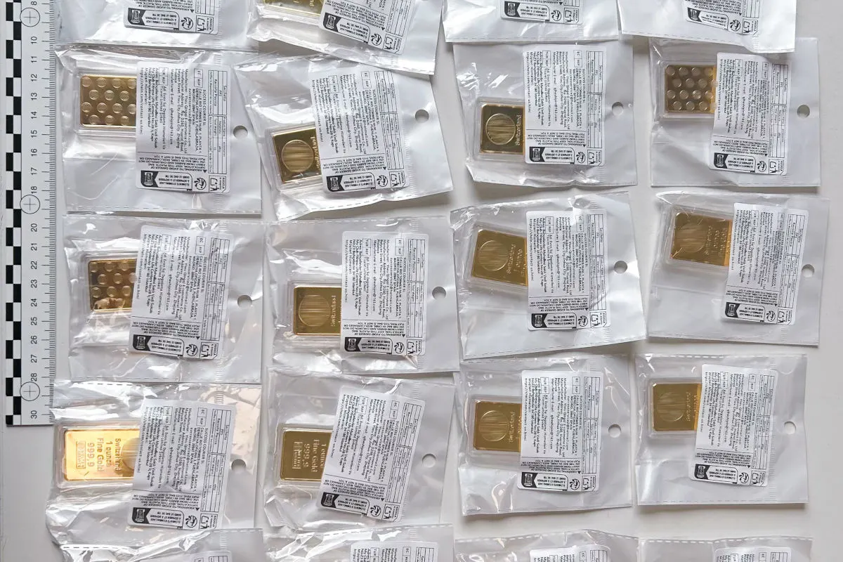 Das Bild zeigt mehrere verpackte Goldbarren, die in dünnen Plastikhüllen auf einer ebenen Fläche angeordnet sind. Neben den Barren ist eine Messskala sichtbar.