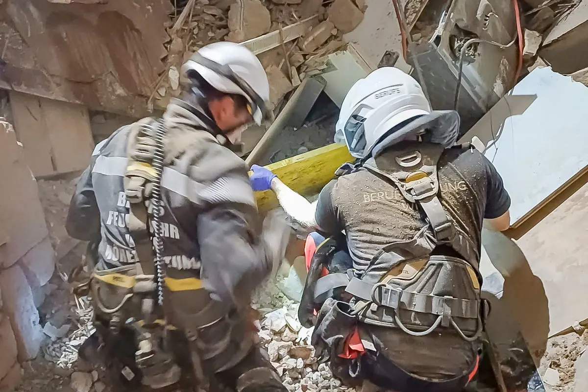 Zwei Feuerwehrmänner in Schutzausrüstung arbeiten in einem zerstörten Gebäude, umgeben von Trümmern.