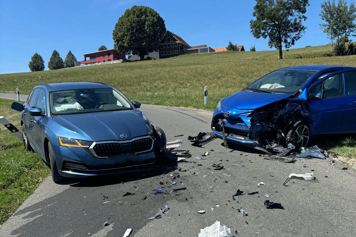 Zwei Autos sind frontal kollidiert und stark beschädigt auf einer ländlichen Straße. Trümmerteile sind auf den Asphalt verstreut.