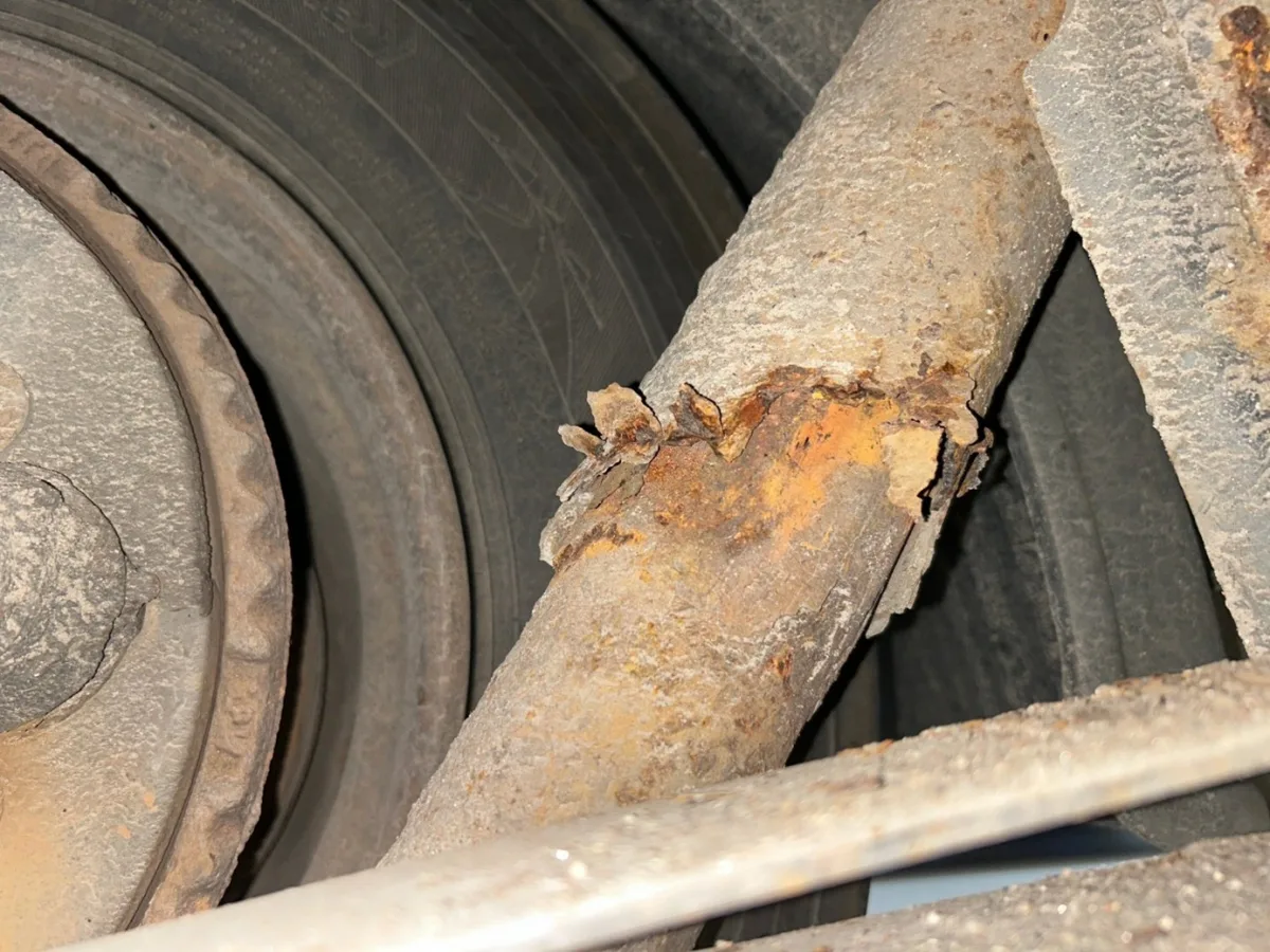 Das Bild zeigt eine Nahaufnahme von stark verrostetem Metall an einem Fahrzeugteil neben einem Rad, was auf strukturellen Verfall hinweist.