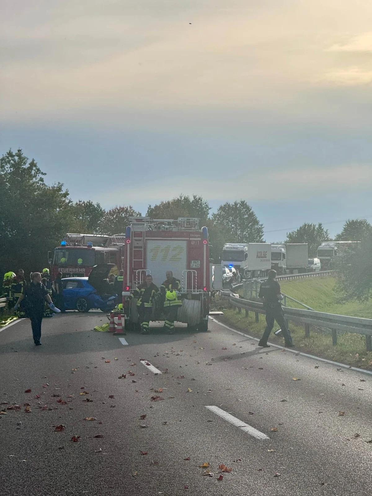 Ein Feuerwehrfahrzeug steht auf einer Autobahn, umgeben von Einsatzkräften in leuchtender Schutzkleidung. Im Hintergrund sind mehrere Fahrzeuge zu sehen.