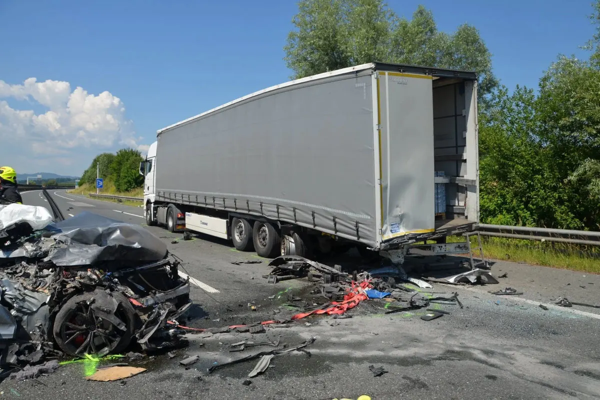 Ein Pkw ist schwer beschädigt nach dem Zusammenstoß mit einem Lkw-Anhänger, der auf der Autobahn steht. Trümmer liegen verstreut auf der Fahrbahn.
