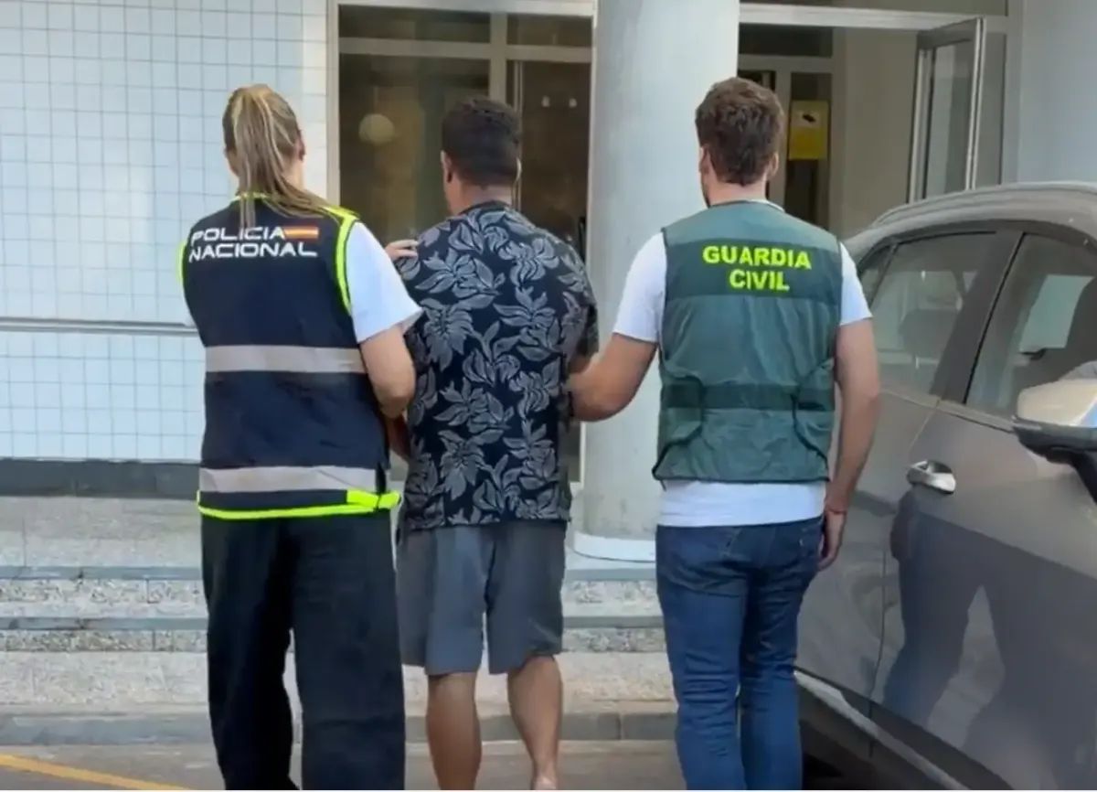 Zwei Polizisten mit Westen der Guardia Civil und Policía Nacional eskortieren einen Mann in ein Gebäude.