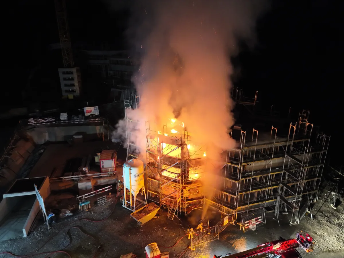 Das Bild zeigt ein Baugerüst bei Nacht, das mit hellen Flammen brennt. Dichter Rauch steigt auf, deutet auf einen intensiven Brand hin.