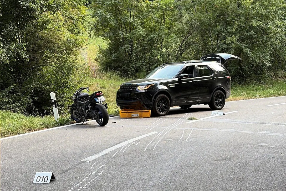 Ein Motorrad und ein SUV sind in einem Unfall verwickelt und stehen auf einer Landstraße. Im Hintergrund ist viel Grün zu sehen.