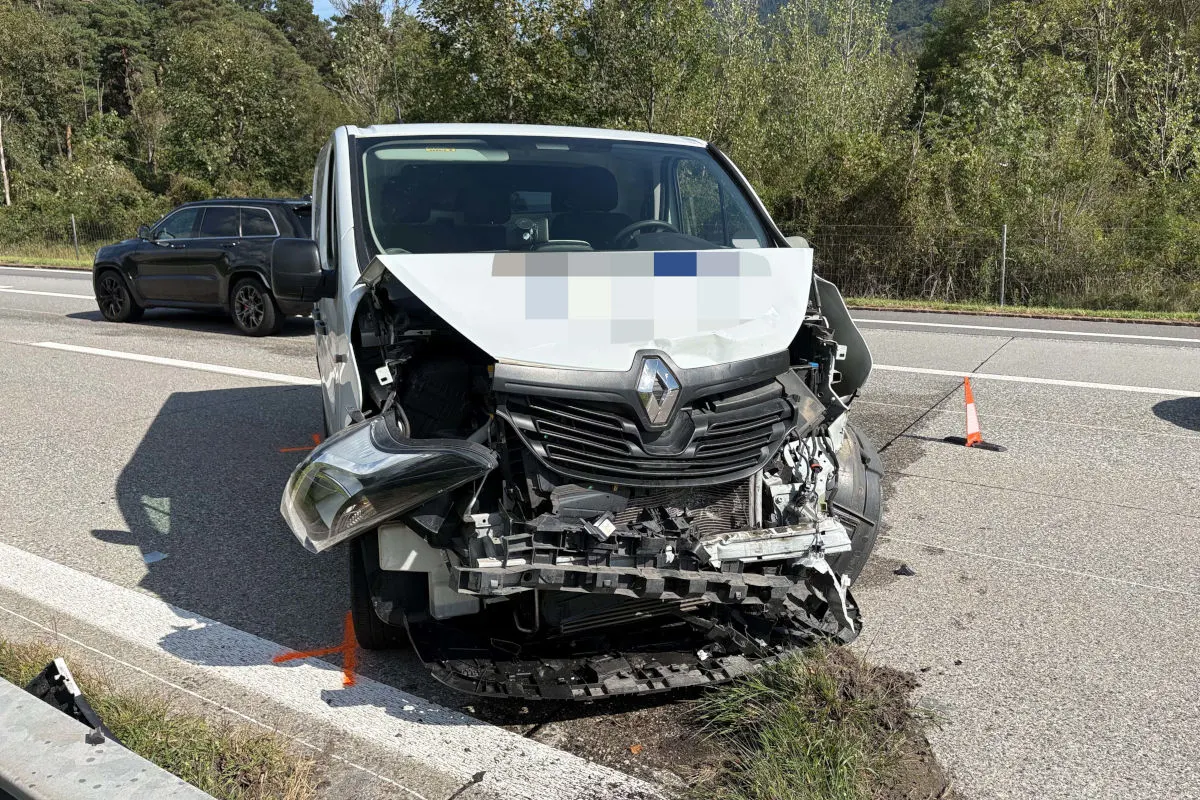 Ein weißer Renault-Transporter steht mit stark beschädigter Front auf einer Autobahn. Ein weiteres schwarzes Fahrzeug befindet sich im Hintergrund, und Pylonen sind auf der Straße sichtbar.