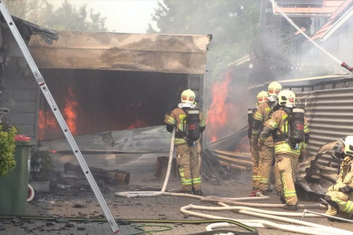 Mehrere Feuerwehrmänner in voller Ausrüstung löschen einen großen Brand in einer Garage. Flammen und Rauch steigen auf.