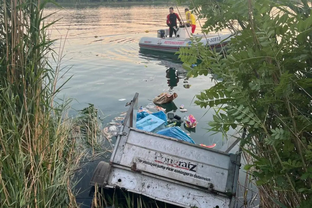 Ein Rettungsboot mit Einsatzkräften ist auf einem See im Einsatz. Im Vordergrund liegt ein Anhänger teilweise im Wasser.