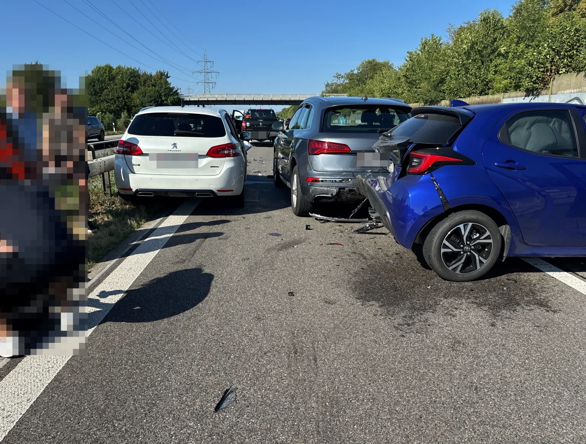 Drei Fahrzeuge mit sichtbaren Beschädigungen stehen auf einer Autobahnspur. Personen sind am linken Bildrand teilweise sichtbar.
