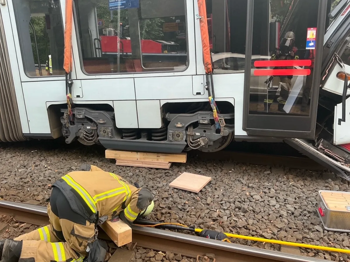Ein Feuerwehrmann in Schutzkleidung arbeitet unter einem entgleisten Zug an den Gleisen, während der Zug auf Holzklötzen gestützt ist.