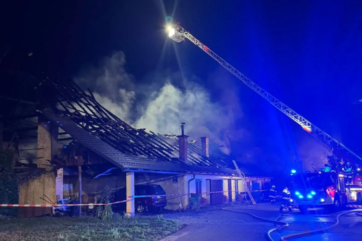 Ein Haus steht nachts in Flammen. Feuerwehrkräfte sind dabei, den Brand zu löschen. Ein Leiterwagen ist im Einsatz.