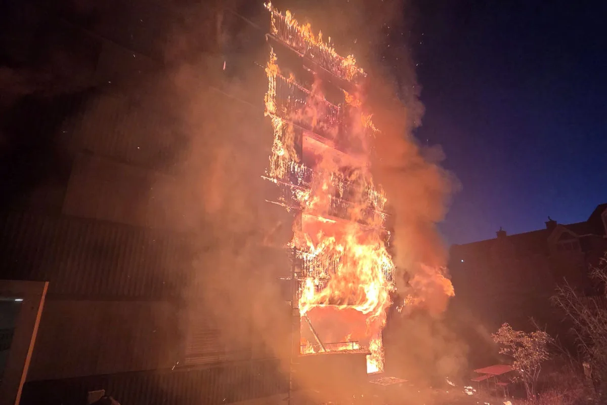 Ein mehrstöckiges Gebäude steht bei Nacht in Flammen und erzeugt dichte Rauchwolken. Das Feuer erhellt die Umgebung in einem intensiven Orange.