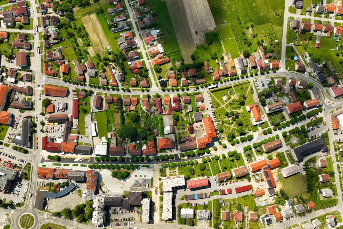 Das Bild zeigt eine Luftaufnahme eines Wohngebiets mit zahlreichen Häusern, geordneten Straßen und vereinzelten Grünflächen. Auch vereinzelte Parkplätze und ein kleiner Park sind zu erkennen.