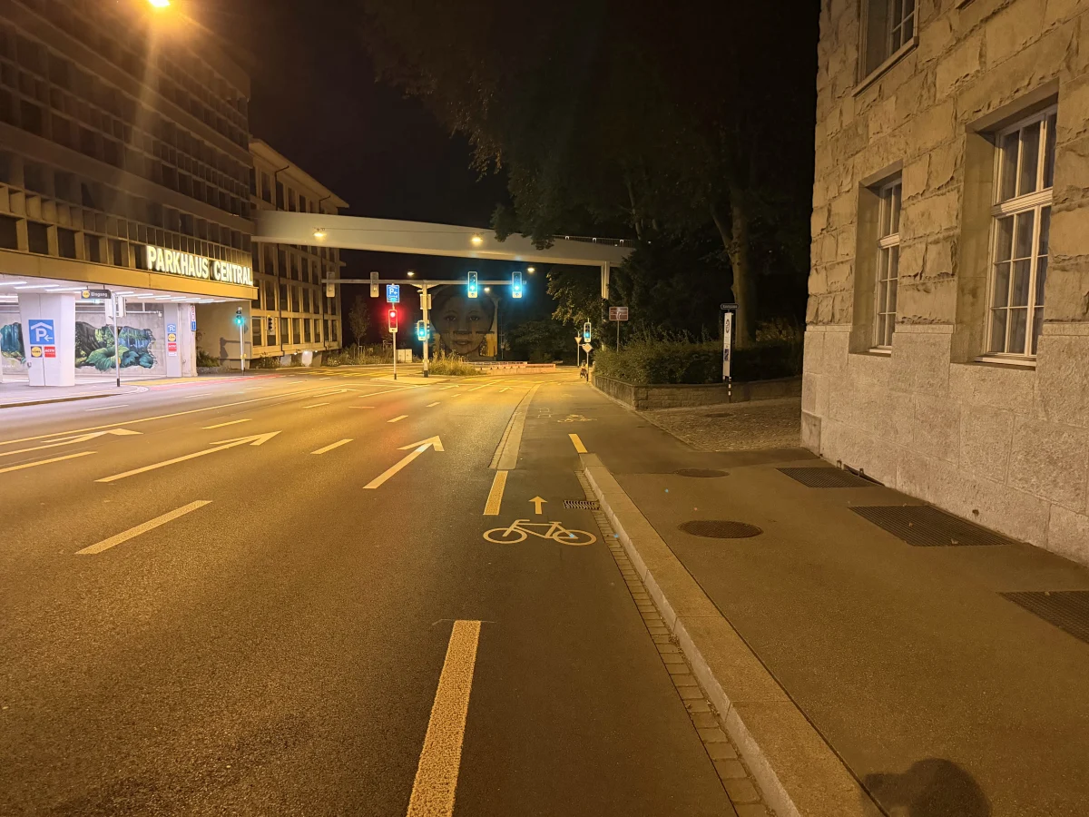 Eine Straße in Zürich bei Nacht, menschenleer, vor einem beleuchteten Parkhaus und einer Ampelanlage.