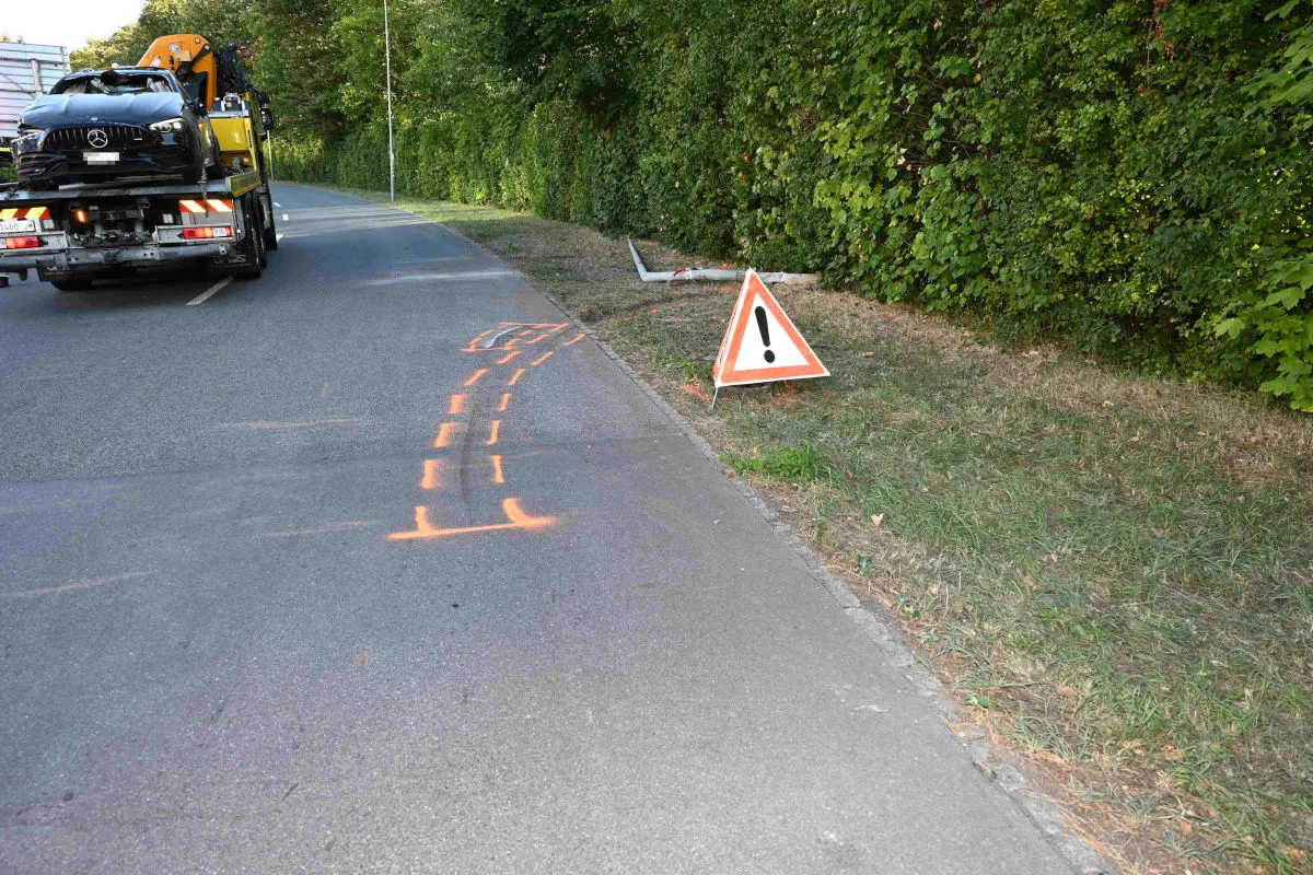 Ein Abschleppfahrzeug transportiert ein Auto auf einer Straße. Am Straßenrand steht ein Warnschild mit einem Ausrufungszeichen.