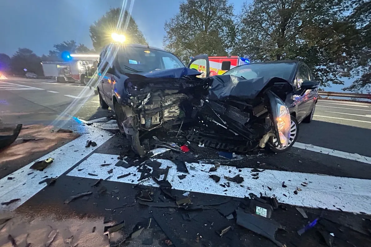 Zwei stark beschädigte Fahrzeuge stehen nach einem Unfall auf einer Straße. Ein Rettungsfahrzeug ist im Hintergrund sichtbar.