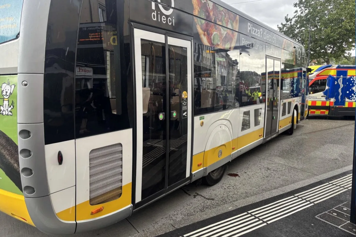 Ein Linienbus mit Werbung steht auf einer Straße. Rechts daneben ist ein Rettungswagen zu sehen. Die Straße scheint nass zu sein.