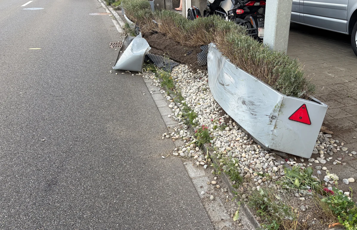 Die Leitplanke ist stark beschädigt, und Erde ist auf den Gehweg verteilt. Im Hintergrund ist ein Straßenszene zu sehen.