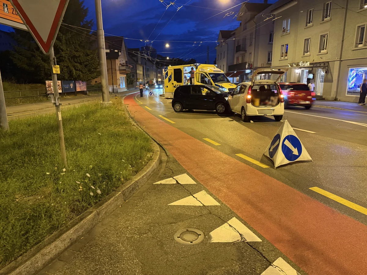 Zwei Fahrzeuge stehen auf einer beleuchteten Straße in einer städtischen Umgebung, begleitet von einem temporären Verkehrsschild.