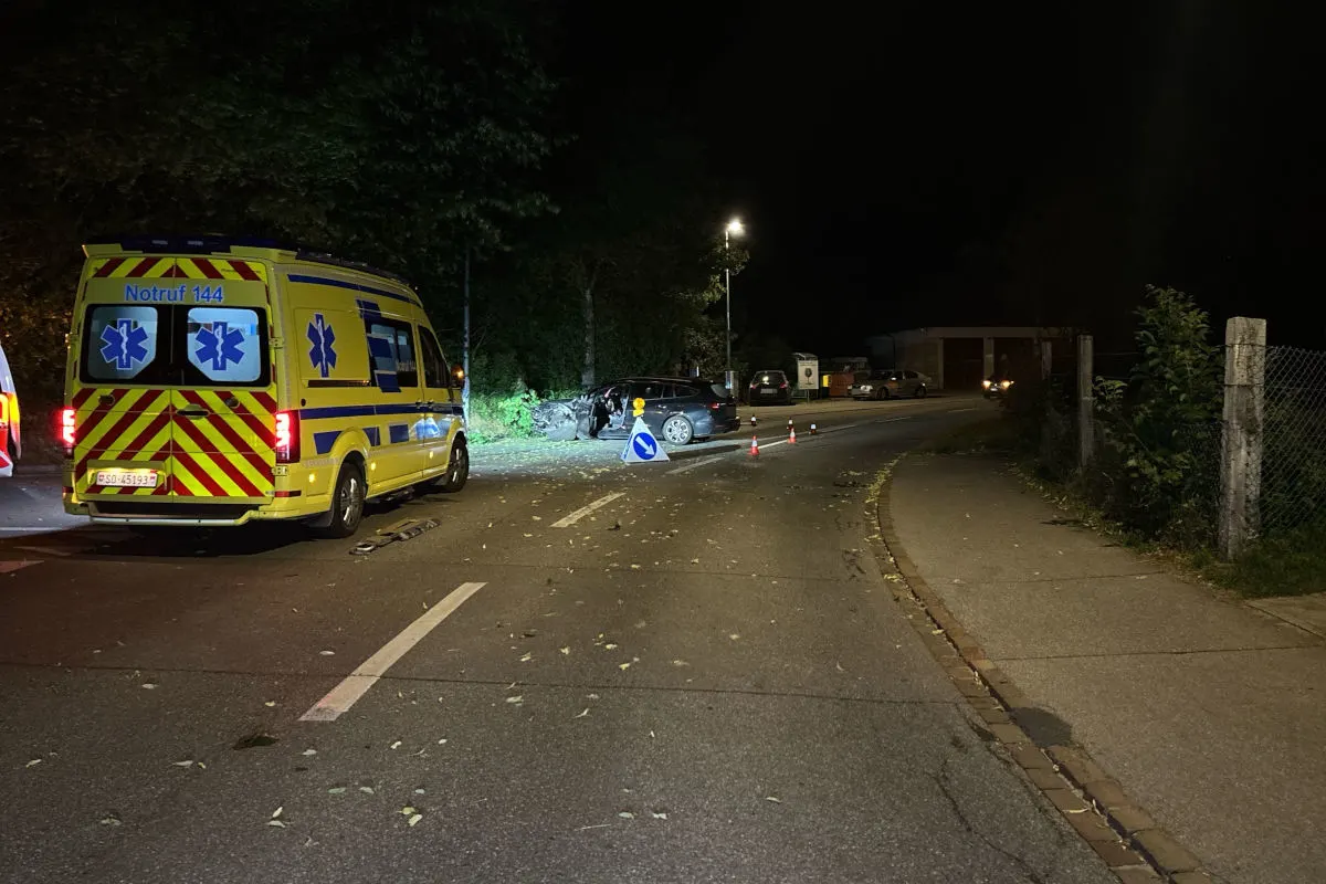 Ein gelbes Rettungsfahrzeug steht auf einer beleuchteten Straße bei Nacht. Eine Unfallstelle ist durch Kegel und Schilder gesichert.