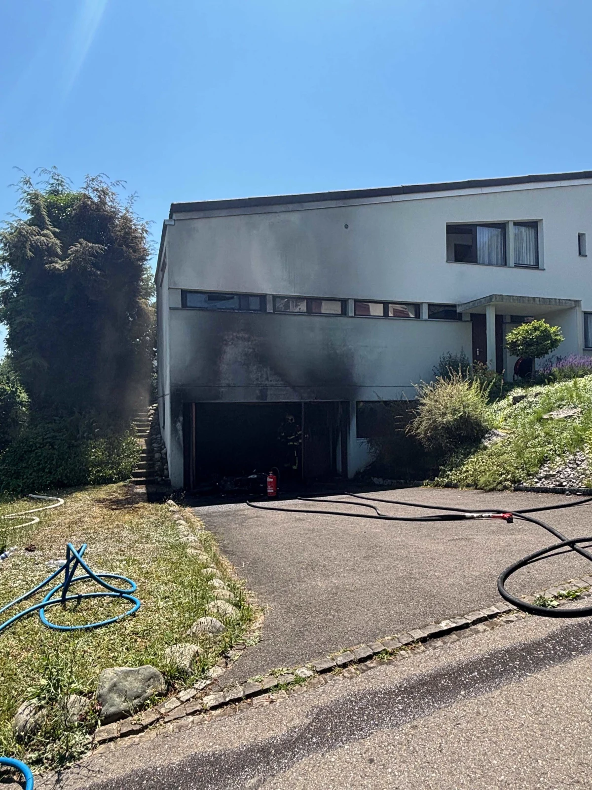 Eine Garage unter einem Wohnhaus ist stark verrußt. Mehrere Schläuche liegen verstreut auf dem Boden.