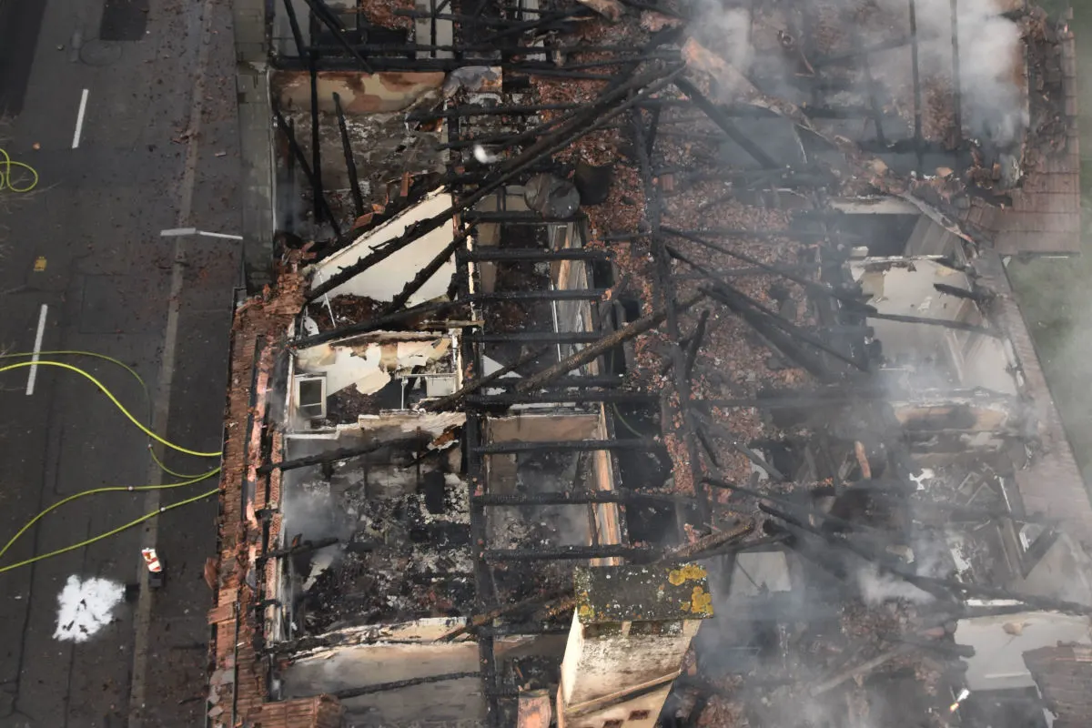 Luftaufnahme eines Gebäudes, dessen Dachgeschoss durch ein Feuer zerstört wurde; verkohlte Balken und Rauch sind sichtbar.