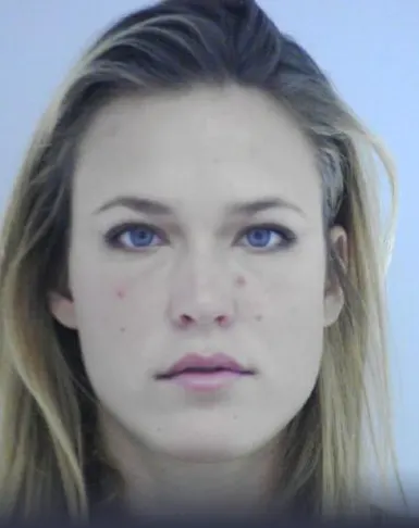 Nahaufnahme einer blonden Frau mit ernstem Gesichtsausdruck vor einem hellblauen Hintergrund.