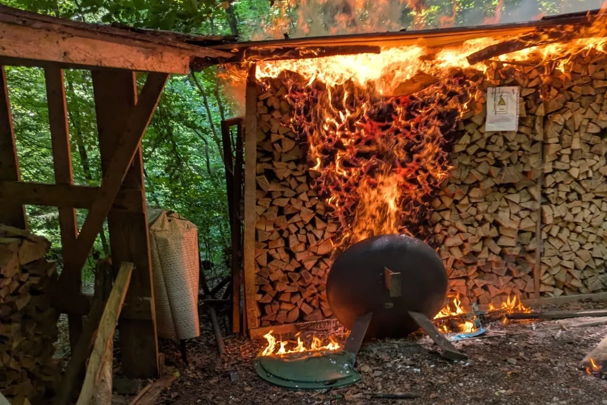 Ein Feuer erfasst einen Holzstapel in einem Unterstand im Wald. Flammen schlagen hoch und bedecken das Dach.