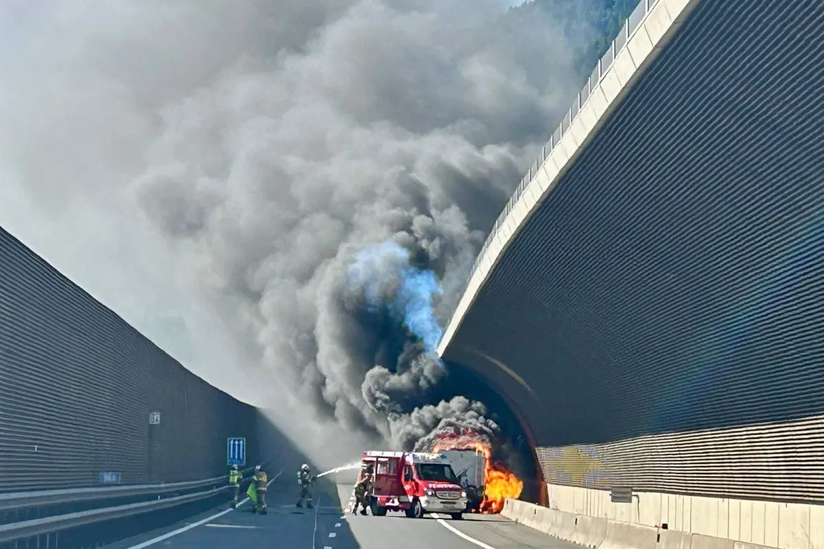 Ein brennender Lkw steht in einem Tunnel, umgeben von dichten Rauchschwaden. Feuerwehrleute sind im Einsatz, um das Feuer zu löschen.