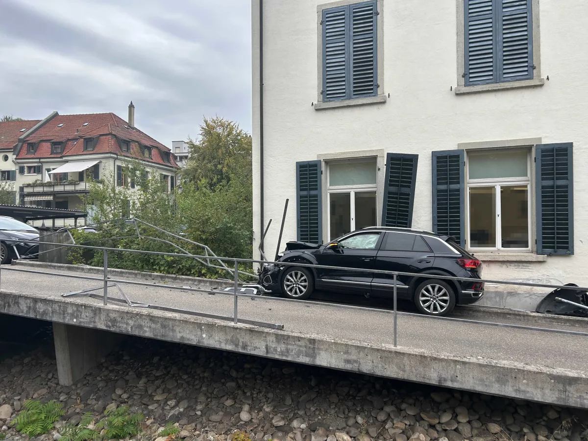 Ein schwarzer SUV ist frontal in ein Haus gefahren. Die Fassade und ein Metallgeländer wurden dabei erheblich beschädigt.