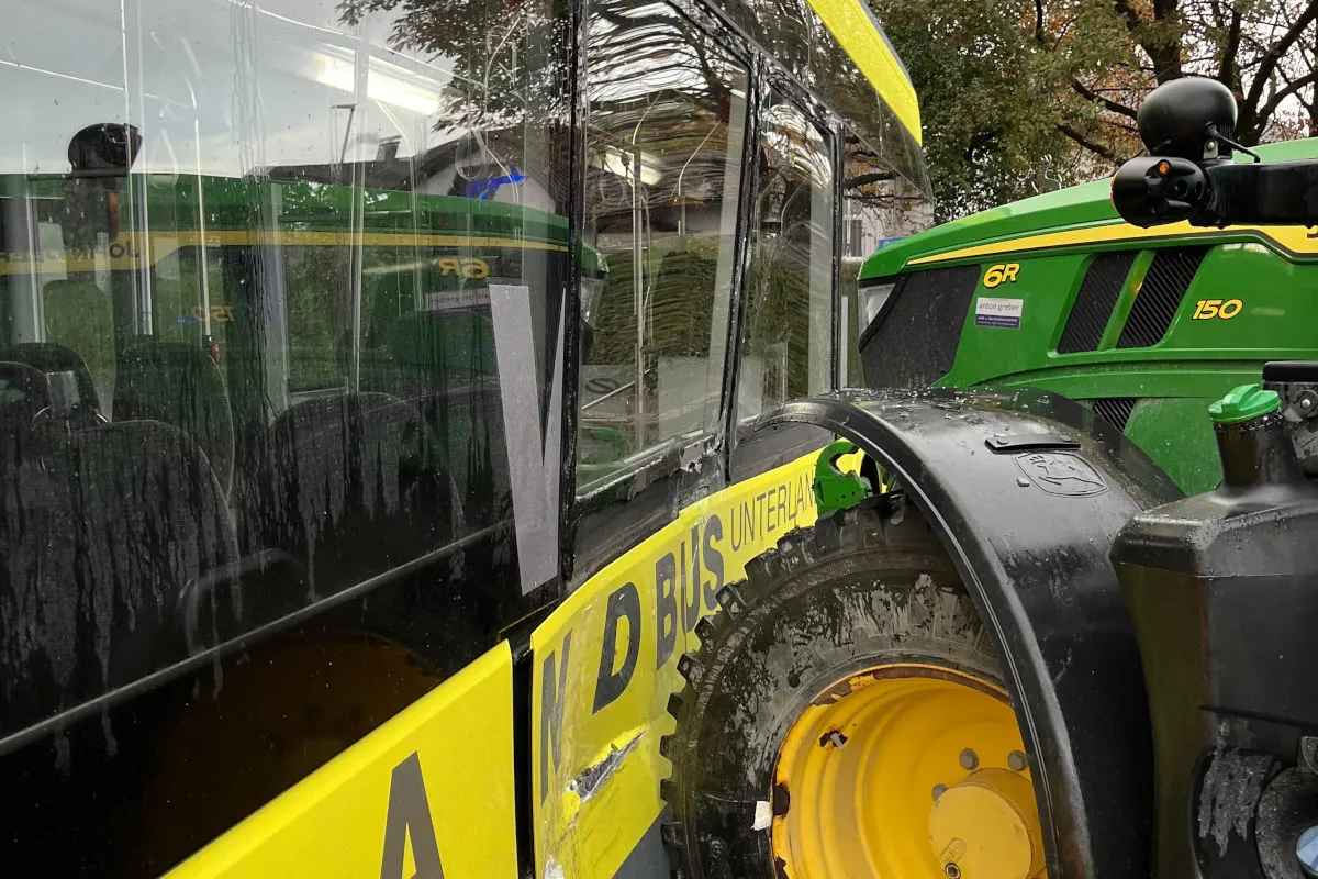Ein gelb-schwarzer Bus und ein grüner Traktor stehen nach einer seitlichen Kollision nah beieinander. Der Bus zeigt sichtbare Lackschäden.