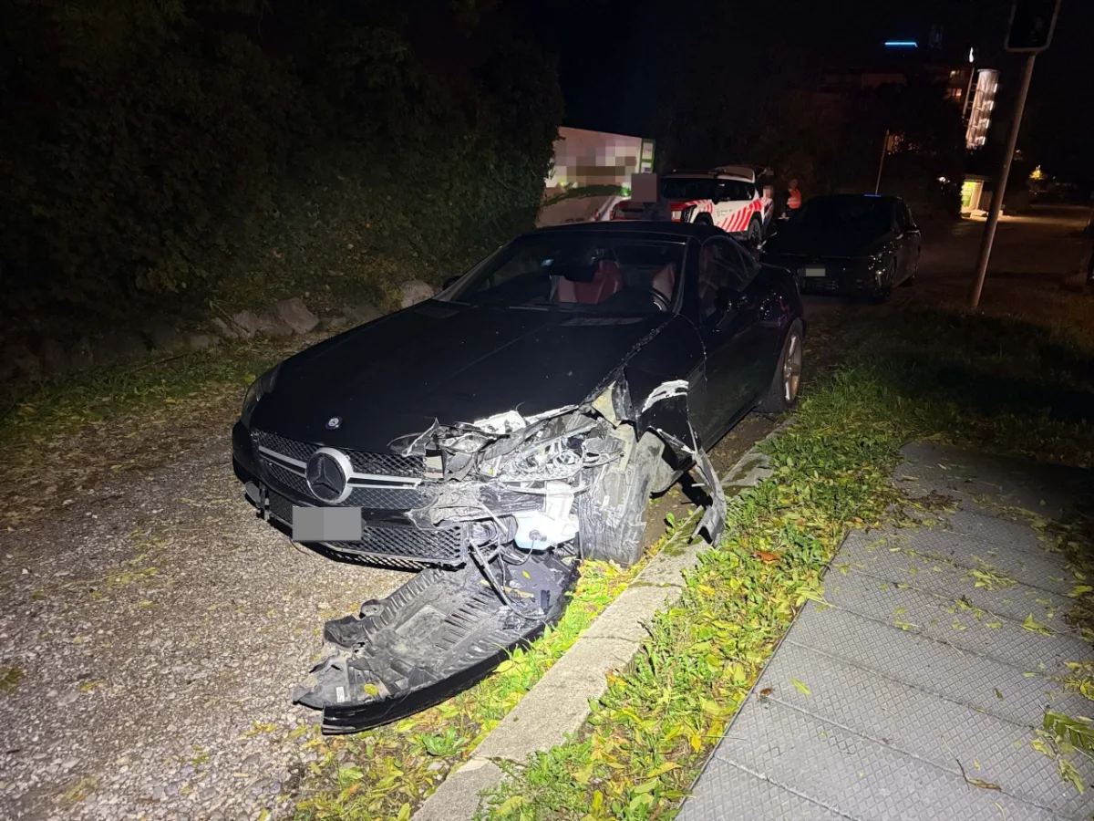 Ein schwarzer Mercedes mit schweren Frontschäden steht bei Nacht am Straßenrand. Laub und Gehwegplatten sind sichtbar.
