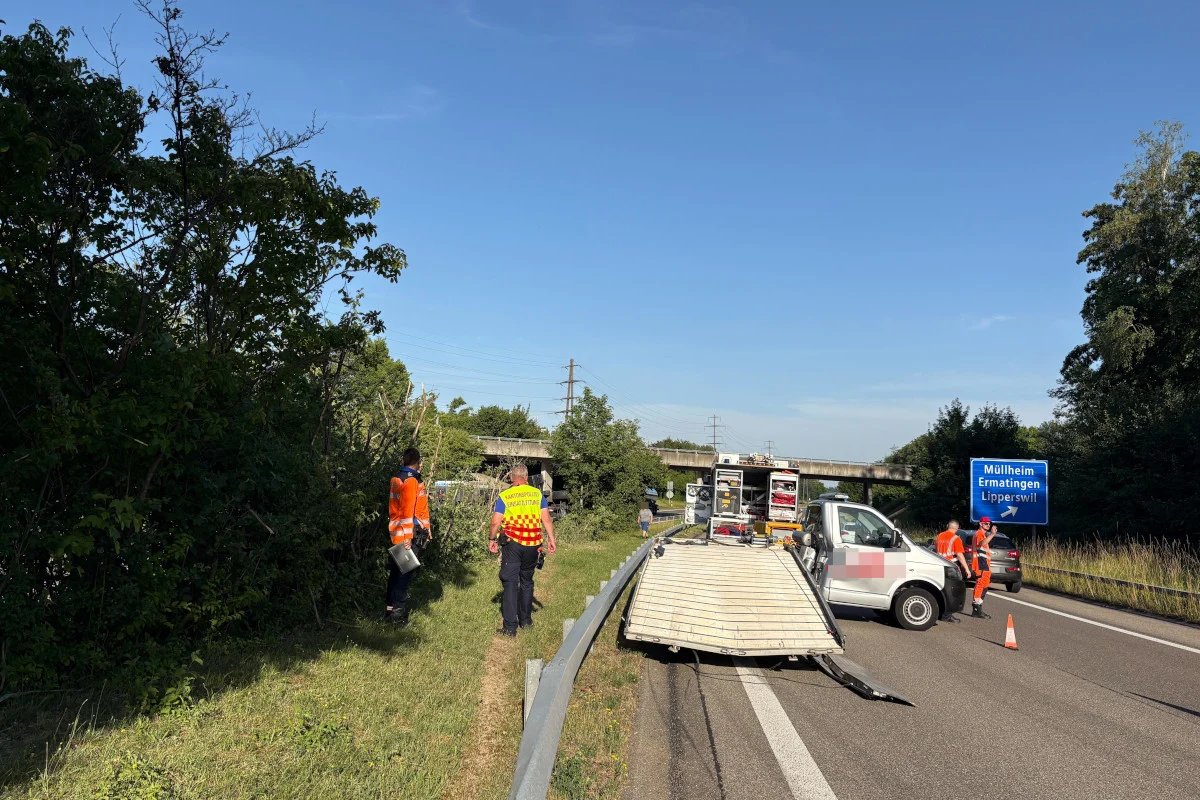 Ein umgekippter Anhänger blockiert die Straße; Polizei und Rettungskräfte sind vor Ort. Im Hintergrund eine Straßenbeschilderung.