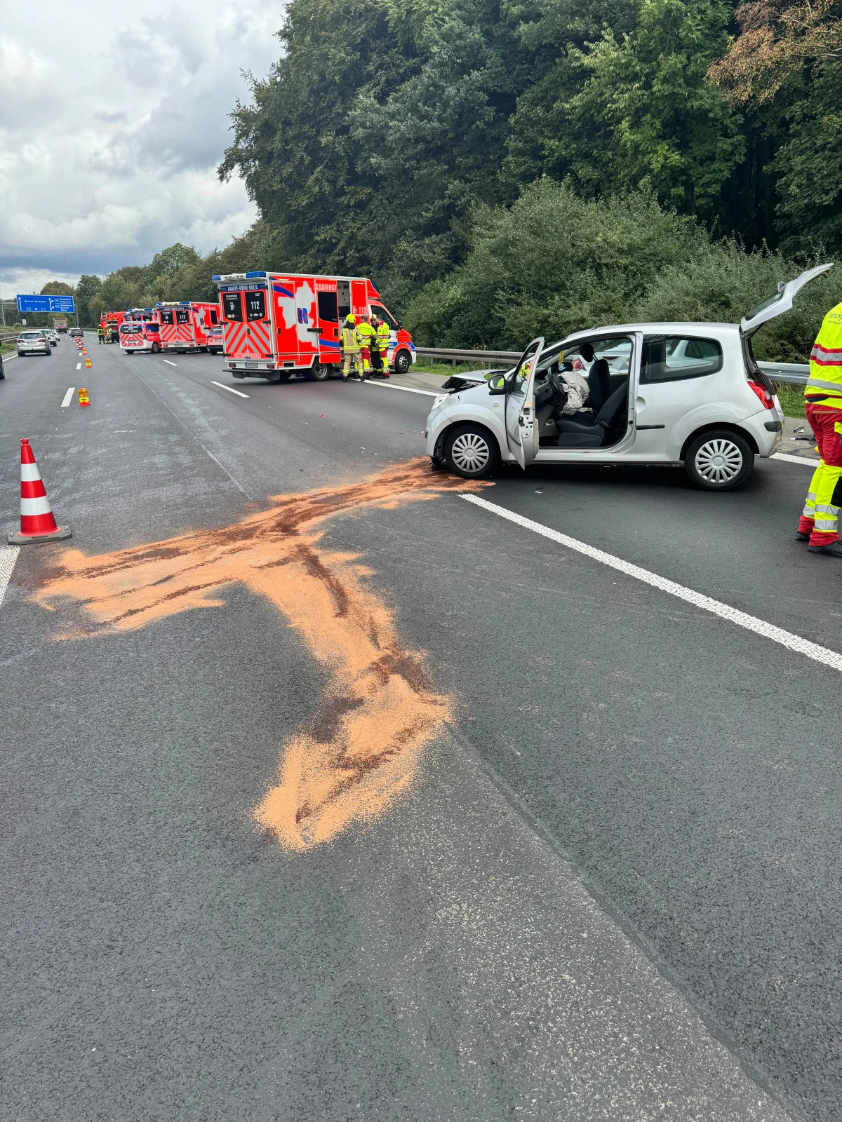 Ein silberner Pkw steht mit geöffneter Tür auf einer Autobahn. Mehrere Rettungsfahrzeuge und Einsatzkräfte sind vor Ort.