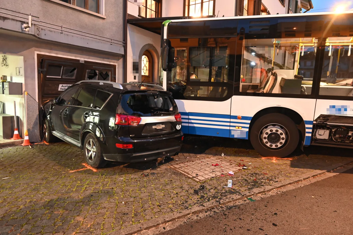 Ein dunkler SUV und ein Linienbus sind in eine Garagenwand gefahren und haben sichtbare Schäden verursacht. Glasscherben und Trümmer sind auf dem Boden verstreut.
