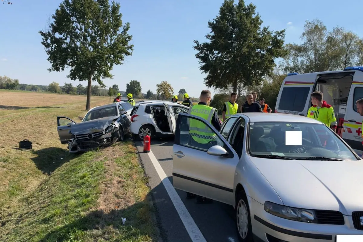 Ein grauer Mercedes und ein weißer Kleinwagen kollidierten auf einer Landstraße. Polizeibeamte und Rettungskräfte sind vor Ort.