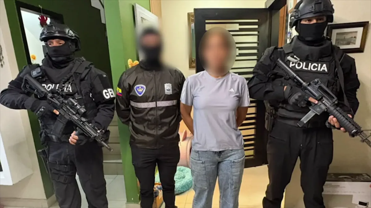 Zwei bewaffnete Polizisten in Uniform halten eine Person in freizeitlicher Kleidung fest. Die Szene spielt sich in einem Innenraum ab.