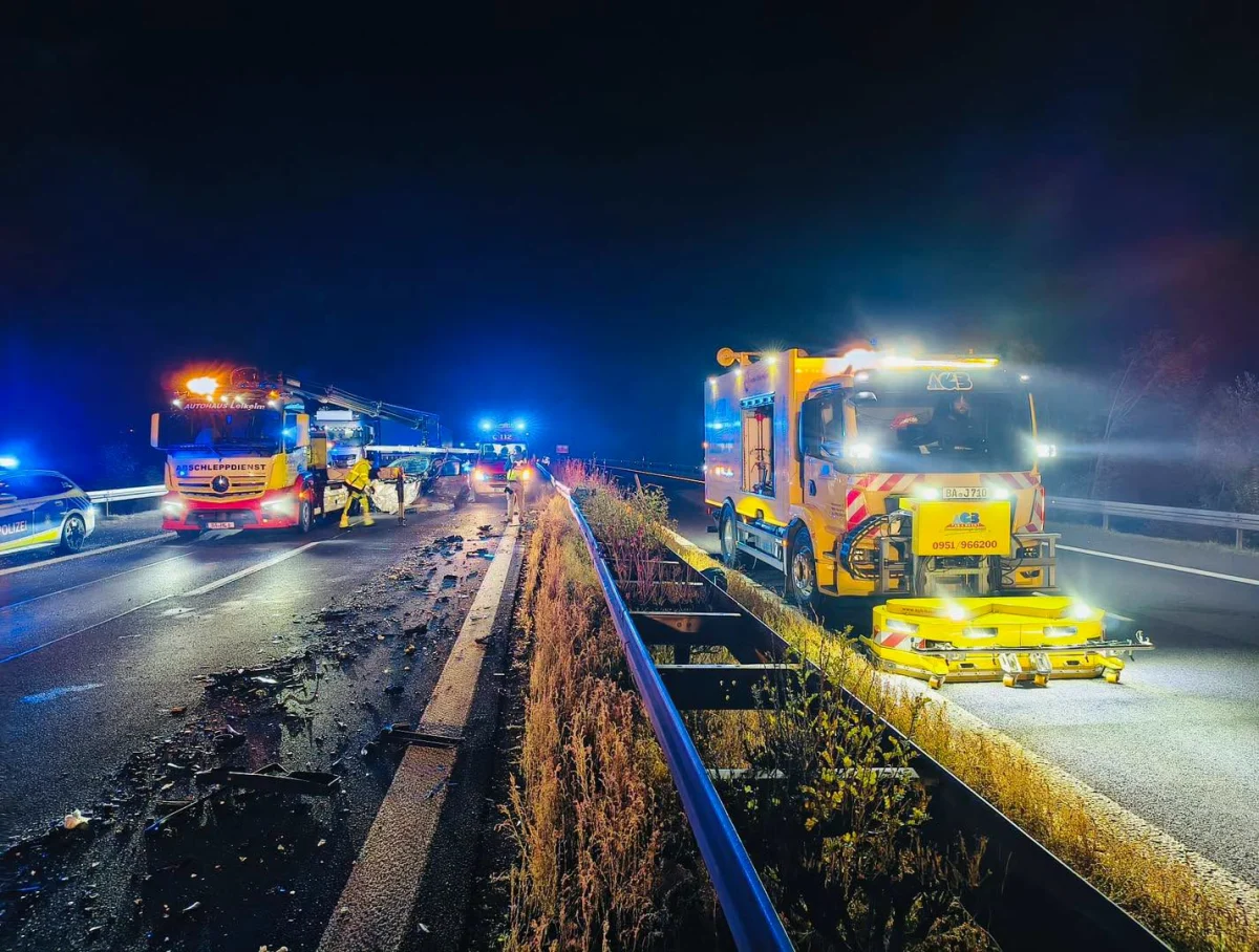 Zu sehen ist eine nächtliche Autobahn mit zwei Einsatzfahrzeugen. Trümmer liegen auf der Fahrbahn, während Einsatzkräfte arbeiten.