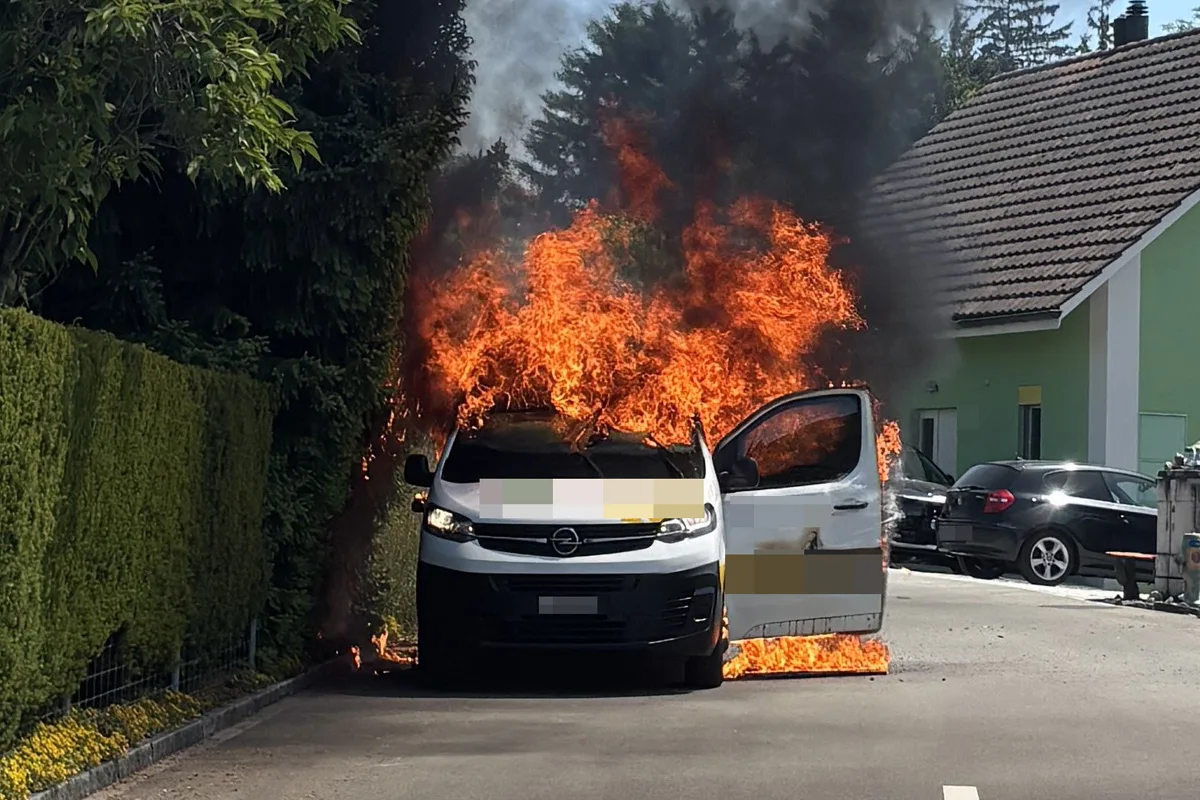 Ein weißer Opel steht lichterloh in Flammen auf einer Straße in einem Wohngebiet. Die Fahrzeugtür ist offen.