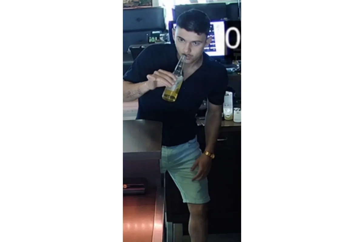 Ein Mann mit dunklen Haaren und dunklem Hemd trinkt aus einer Flasche. Er steht an einer Theke mit technischer Ausrüstung.