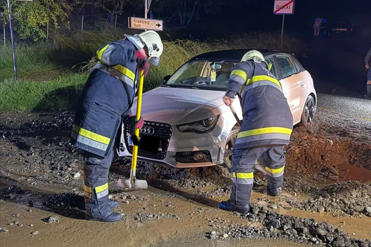 Zwei Feuerwehrleute arbeiten nachts daran, einen silbernen Audi aus einem Erdloch zu bergen. Der Boden ist nass und schlammig.