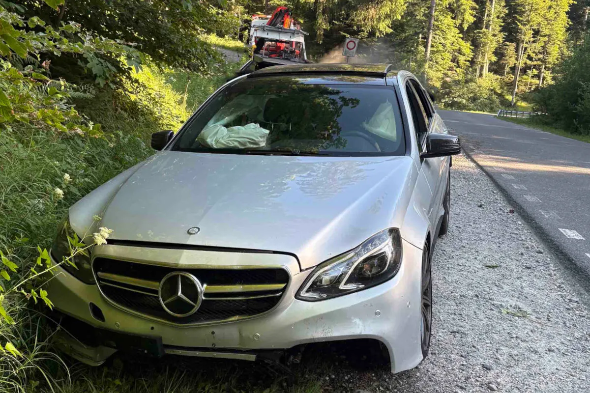 Ein weißer Mercedes steht mit offenem Airbag und beschädigtem Frontbereich am Straßenrand. Im Hintergrund ist ein Abschleppfahrzeug zu sehen.