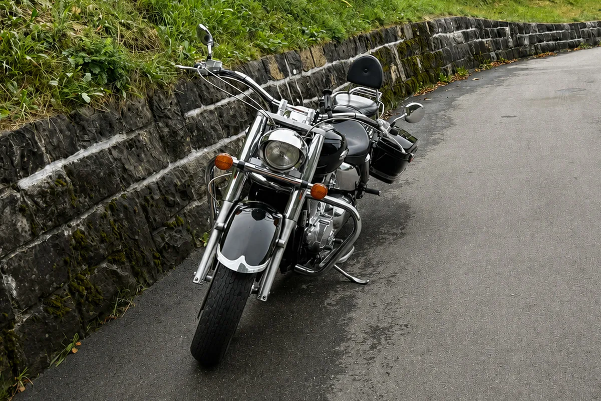 Ein größeres Motorrad steht abgestellt auf einer schmalen Straße. Links daneben verläuft eine Steinmauer mit Vegetation.