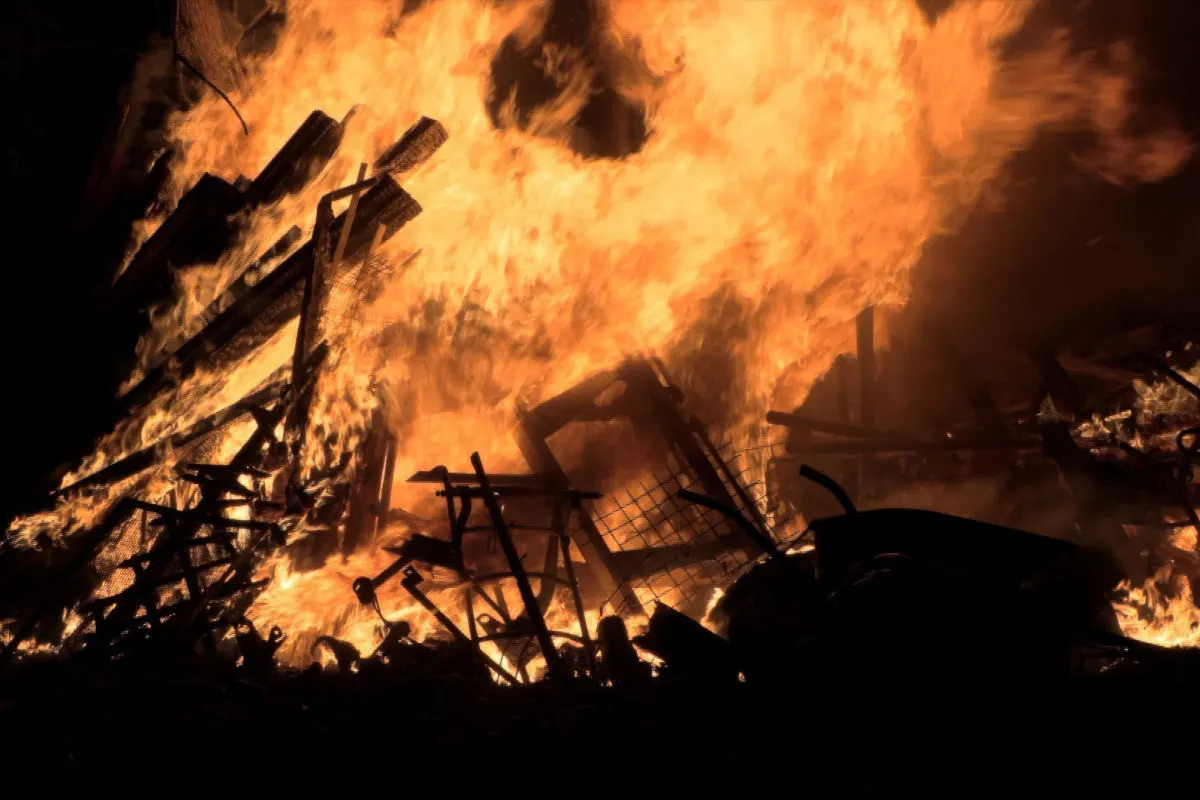 Ein intensives Feuer vernichtet eine Ansammlung von Holzkonstruktionen und verschiedenen Trümmerteilen bei Nacht.