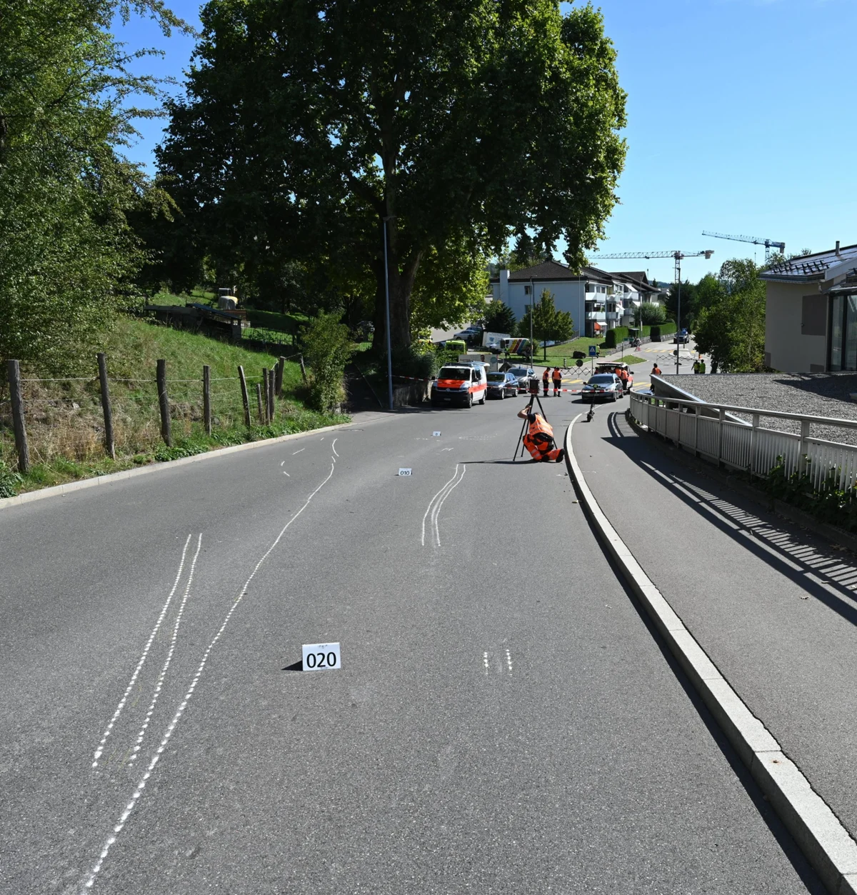 Auf einer Landstraße sind Markierungen für eine Unfalluntersuchung sichtbar, mit Absperrungen und Ermittlern im Hintergrund.