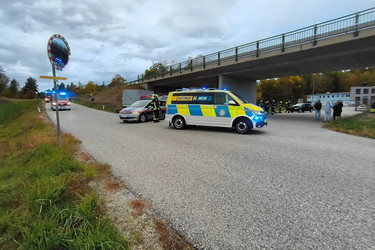 Ein Feuerwehrfahrzeug steht auf einer Landstraße unter einer Brücke, umgeben von Einsatzkräften und weiteren Fahrzeugen.