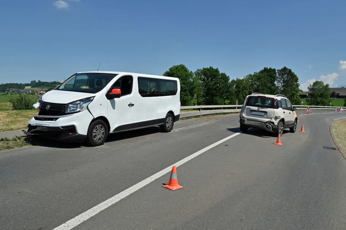 Ein weißer Van und ein blauer SUV sind nach einem Auffahrunfall auf einer Landstraße beschädigt. Verkehrsleitkegel kennzeichnen die Unfallstelle.