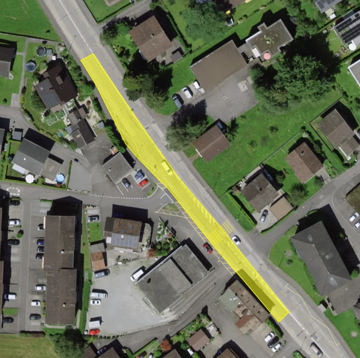 Luftaufnahme eines markierten Straßenabschnitts in einem Wohngebiet mit mehreren Häusern und Autos. Der markierte Bereich hebt sich in Gelb hervor und zieht sich über eine Straße.